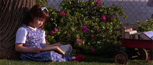 Matilda leyendo un libro sentada de bajo de un árbol